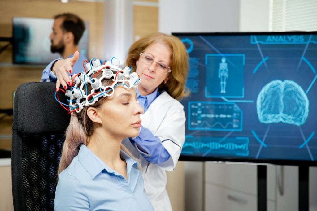 Doctor arranging neurology scanning headset for tests on a female patient